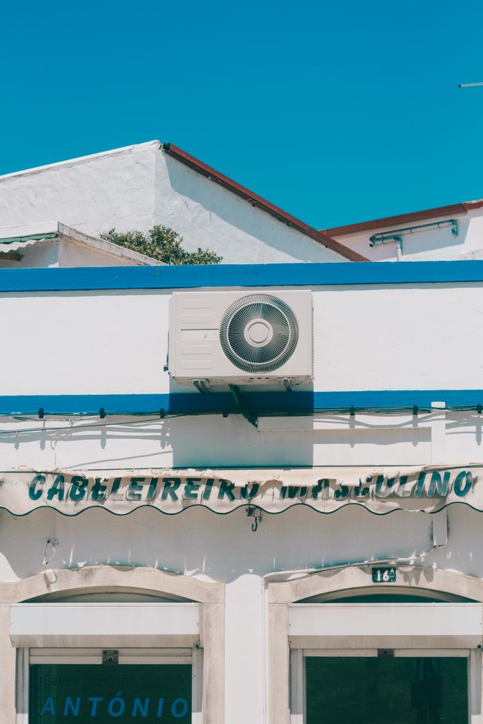 Services Exterior view of a modern hair salon with visible air conditioning unit under a clear sky.