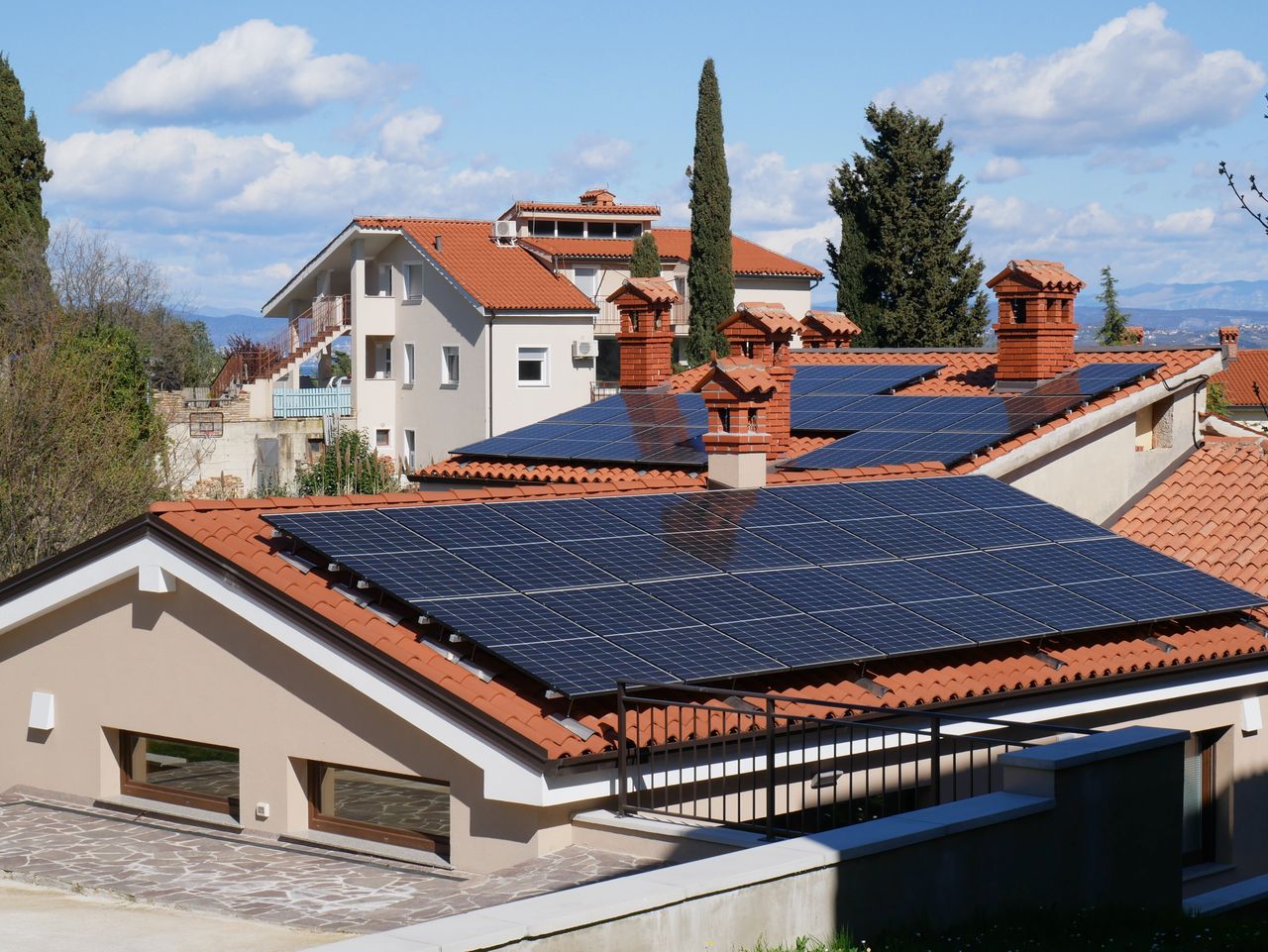Services A panoramic view of solar panels on red tile rooftops in a sunny suburban neighborhood.